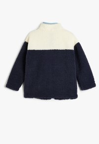 Fleece-pullover med hög krage, i halva krämfärg och halva marinblå i färgblockdesign. Mjuk textur och lös passform, med rundade kanter vid fållen.