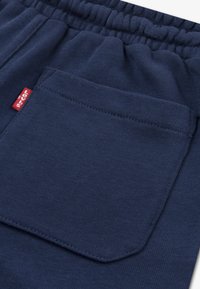 Jogging en coton bleu marine avec une taille élastique, des poches latérales et une poche arrière rectangulaire avec une étiquette de marque rouge.