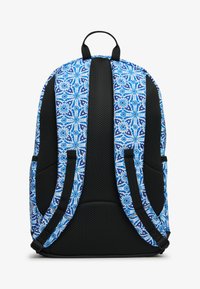 Mochila con un patrón floral azul y blanco, acolchado de malla negra, correas ajustables y bolsillos laterales. Presenta un asa en la parte superior para llevar.