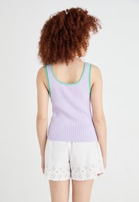 Lilla ribbet tanktop med grønne detaljer, har en tettsittende design. Kombinert med hvite shorts dekorert med blonder.