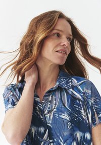 Camicia button-up con un motivo floreale astratto blu e bianco. Maniche corte, tessuto leggero e una texture morbida.