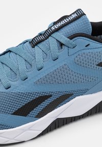 Plava atletska cipela s mrežastim i sintetičkim materijalima, teksturiranom površinom, crnim detaljima i bijelim gumenim potplatom. Reebok logo na vrhu.