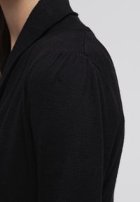 Schwarzer Strickpullover mit einem strukturierten Kragen, gepufften Ärmeln und einer weichen Textur. Der Stoff wirkt leicht und bequem.