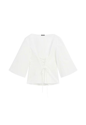 Blouse blanche à manches longues avec de larges manches et un détail de laçage au dos noué en un nœud à la taille.