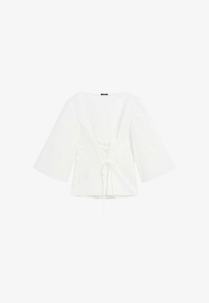 Blouse blanche à manches longues avec de larges manches et un détail de laçage au dos noué en un nœud à la taille.