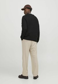 Black textured knit sweater, beige trousers, brown cap, dark shoes; shown from the back, highlighting garment and color contrast.