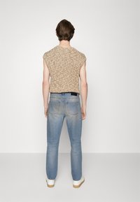 Brunprickig stickad ärmlös topp, blå urtvättade jeans med bakfickor, och vita skor med beige sulor, sedd bakifrån.