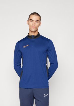 Blauw sporttop met lange mouwen en een ritssluiting bij de kraag, zwarte accenten, oranje Nike-logo en een gladde textuur, gecombineerd met marineblauwe broek.