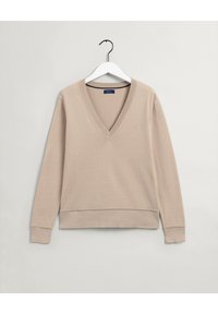 Beige lange mouw V-hals trui met ribgebreide manchetten en zoom, hangend aan een witte hanger tegen een effen lichte achtergrond.