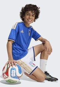 Blue Adidas soccer jersey with gold accents, short white shorts featuring Italian flag and logo, a soccer ball held in hand, and black cleats.