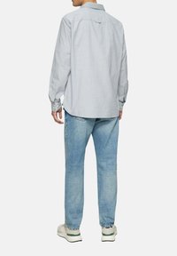 Lichtgrijs overhemd met lange mouwen en een button-down kraag, gecombineerd met vervaagde blauwe jeans en witte sneakers. De achterkant toont stikdetails.