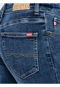 Közeli kép kék farmernadrágról, amelyen a hátsó zseb látható piros Big Star logós címkékkel és részletes varrással a szöveten.