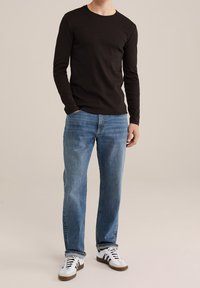 Svart långärmad skjorta, blå denimjeans, vita sneakers med svarta detaljer. Enkel design, vanlig passform och textilväv.