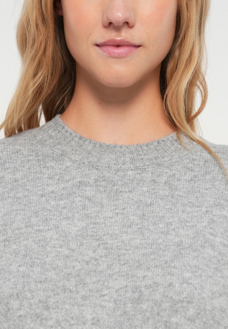 Szary sweter z okrągłym dekoltem, wykonany z miękkiej dzianiny. Posiada ribbowe wykończenie kołnierza oraz gładką teksturę.