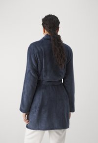 Marinblå fleecekappa med bälte, långa ärmar och sjalkrage. Mjuk textur och medellång design. Skräddarsydd passform vid midjan.