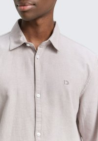Lichtgrijze button-up blouse gemaakt van zachte stof. Kenmerkt zich door een klassieke kraag, witte knopen en een subtiele logo op de borst.