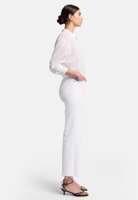 Camicia bianca trasparente con bottoni e maniche lunghe, abbinata a jeans bianchi a vita alta con orlo sfilacciato. Sandali con tacco neri e cinturini.