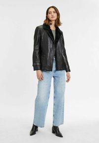Zwarte leren jas met een zachte zwarte bontkraag, gecombineerd met lichtblauwe, wijde jeans met studs.