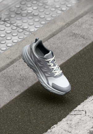 Lightweight athletic shoe in gray and white, with a mesh upper, textured sole, and contrasting rubber accents. Features flat laces and a rear pull tab.