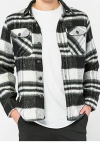 Svart- och vitrutigt flanellskjorta med två bröstfickor, knappad fram, och standardkrage, bärs över en vit t-shirt.