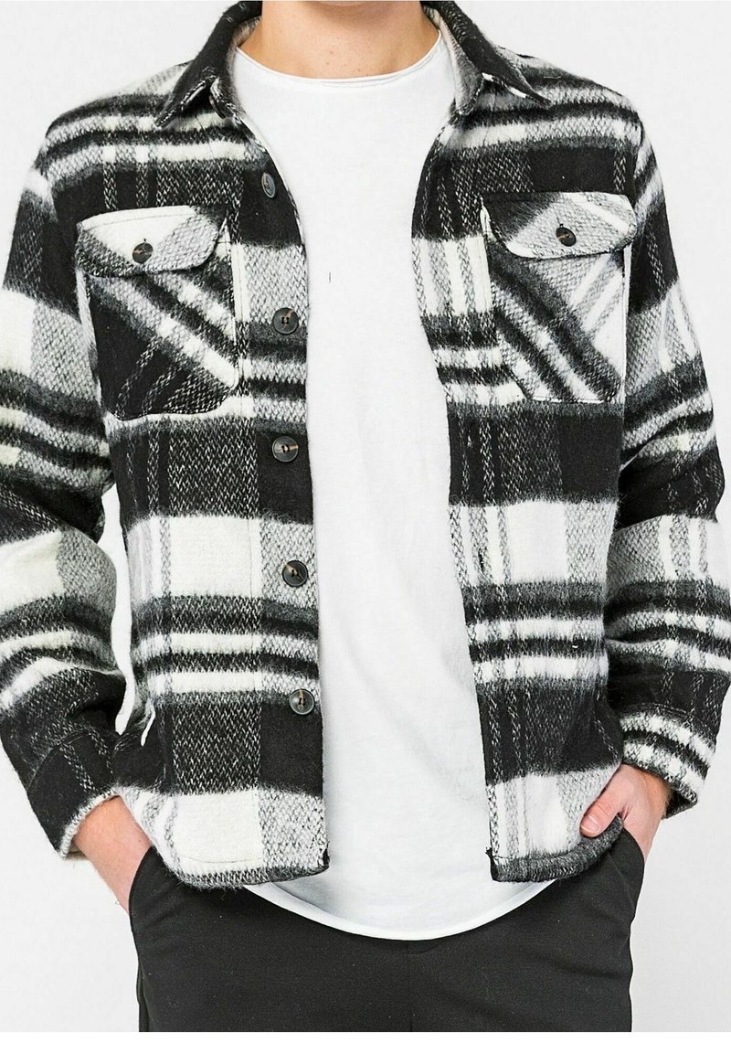 Svart- och vitrutigt flanellskjorta med två bröstfickor, knappad fram, och standardkrage, bärs över en vit t-shirt.