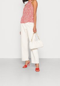 Top halter rosso a fiori, pantaloni bianchi a gamba larga, sandali con tacco rosso e una borsa bianca con catena dorata. Texture liscia, design casual.