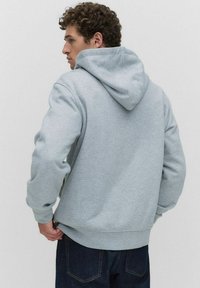Sweatshirt à capuche gris en mélange de coton, avec une poche kangourou et des poignets côtelés. Texture lisse et design à coupe décontractée.