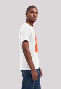 White cotton t-shirt featuring a colorful abstract design in red and orange hues on the front, short sleeves, and a crew neckline.