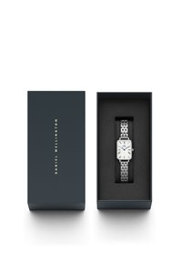 Montre rectangulaire en argent avec un cadran blanc, des aiguilles bleues et des chiffres romains, présentée dans une boîte bleu foncé avec un rembourrage noir.