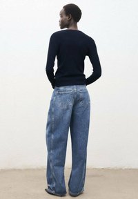 Navy Pullover aus Strick kombiniert mit hellblauen weit geschnittenen Denim-Jeans. Die Jeans verfügen über Gesäßtaschen und sind locker geschnitten. Einfarbiger weißer Hintergrund.