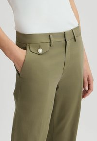 Pantaloni verde oliva con una texture liscia, dotati di una tasca laterale con un bottone decorativo in perla e una vita aderente.