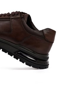 Bruine leren sneaker met geperforeerde details, een gevoerde kraag en een dikke zwarte rubberen zool met een slank luchtkussenontwerp.