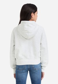 Svetlošedá mikina s voľným strihom, ktorá má kapucňu a rebrované manžety. V páre s modrými džínsami, zobrazená z bočnej strany a s čistými líniami.