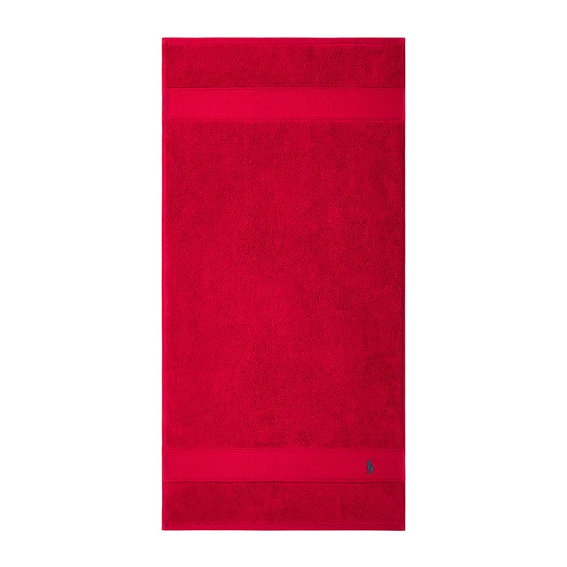 Κόκκινη βαμβακερή πετσέτα μπάνιου με υφασμάτινη υφή, διπλή λωρίδα στην κορυφή και μικρό λογότυπο στην κάτω γωνία.