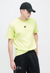 Λαχανί βαμβακερό t-shirt με στρογγυλή λαιμόκοψη και κοντά μανίκια, με μικρό μαύρο λογότυπο Nike στο στήθος, σε συνδυασμό με μαύρο παντελόνι φόρμας.