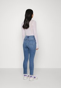 Calças de ganga justas azuis de cintura alta, combinadas com uma blusa justa de mangas longas brancas e ténis brancos com detalhes roxos.