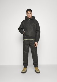 Sudadera con capucha gris y bolsillo canguro sobre una camiseta verde y pantalones grises a juego, combinada con zapatillas gruesas en verde olivo y amarillo.