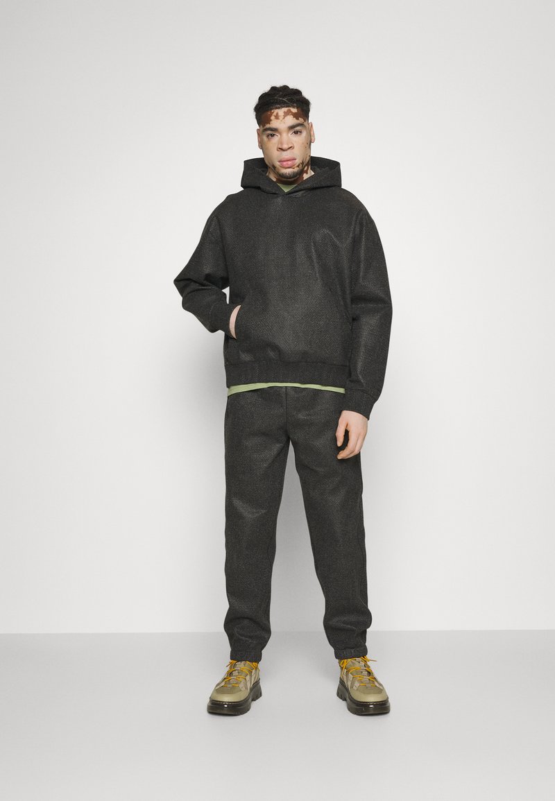 Sudadera con capucha gris y bolsillo canguro sobre una camiseta verde y pantalones grises a juego, combinada con zapatillas gruesas en verde olivo y amarillo.