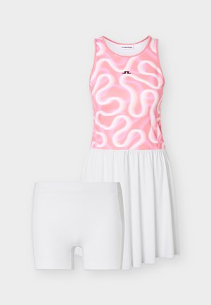Ružičasta i bijela teniska haljina bez rukava s apstraktnim uzorkom kovrča u kombinaciji s jednobojnim bijelim kompresijskim kratkim hlačicama.