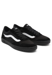 Black sneakers with a combination of suede and mesh materials, featuring a white wave logo, flat laces, and a rubber sole.