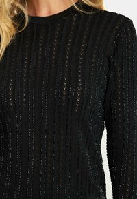 Czarny sweter robiony na drutach z pionowymi paskami i małymi wycięciami. Okrągły dekolt i długie rękawy z fakturowanym wykończeniem.