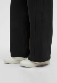 Pantaloni neri a gamba larga con cuciture a vista abbinati a scarpe bianche con superficie liscia e design a punta rotonda.