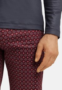 T-paita pitkähihaisena tummansinisenä yhdistettynä tiukkoihin burgundinvärisiin leggings-housuihin, joissa on geometrisia muotoja punaisilla, valkoisilla ja sinisillä korostusväreillä.