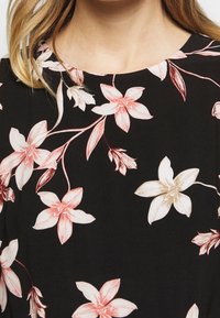 Svart klänning med blommönster i rosa och vitt med gröna accenter och rund halsringning. Slätt tyg med avslappnad passform.