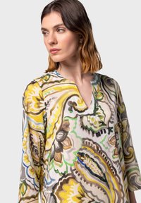 Blusa a maniche lunghe con scollo a V, caratterizzata da un vivace motivo floreale e paisley in tonalità di giallo, verde, marrone e blu su uno sfondo chiaro.