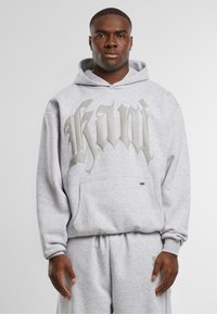 Gray hoodie with a large, metallic silver logo, featuring a front pocket and drawstring hood, paired with matching sweat shorts.