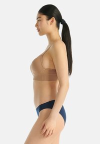 Nude bralette met een gladde textuur en smalle bandjes, gecombineerd met donkere blauwe low-rise slipjes, weergegeven op een model in profiel.