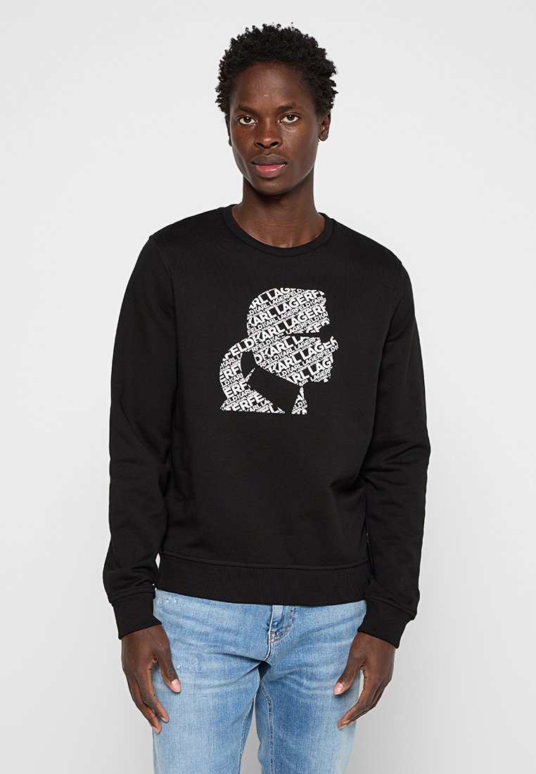 Sudadera negra con cuello redondo y puños acanalados. Presenta un diseño gráfico blanco con texto en forma de silueta en la parte frontal.