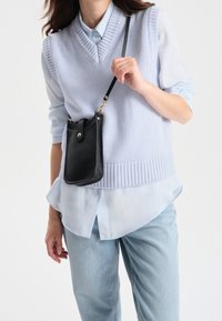 Chaleco de punto azul claro con escote en V, utilizado sobre una camisa de botones azul clara. Bolso cruzado de cuero negro con correa y cierre a presión.