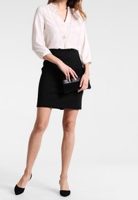 Ljusrosa blus med V-ringning och 3/4-långa ärmar, i kombination med en svart tajt kjol. En svart clutch och svarta pumps med spetsig tå fulländar looken.